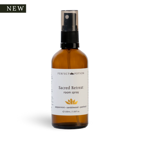A 100ml amber glass room spray bottle with a black spray nozzle and a white label reading 'PERFECT POTION Sacred Retreat room spray'. A black 'NEW' badge is in the top-left corner on a white background.