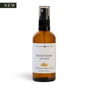 A 100ml amber glass room spray bottle with a black spray nozzle and a white label reading 'PERFECT POTION Sacred Temple room spray'. A small black 'NEW' badge is in the top-left corner on a white background.